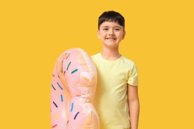 Sarı arka planda şişme yüzük tutan sevimli küçük çocuk.