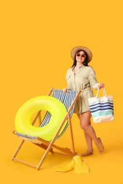 Sarı arka planda şişirilebilir yüzüklü, yüzgeçli ve şezlonglu güzel bir kadın.