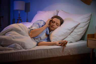 Young woman with sleeping pills suffering from insomnia in dark bedroom clipart