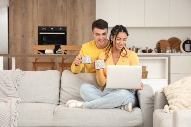 Mutfakta dizüstü bilgisayar kullanan kahve içen genç bir çift.