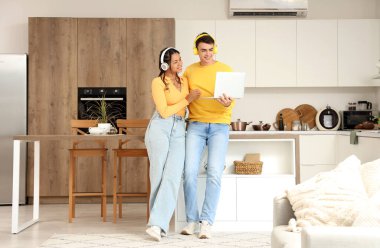 Kulaklıklı genç çift mutfakta dizüstü bilgisayar kullanıyor.