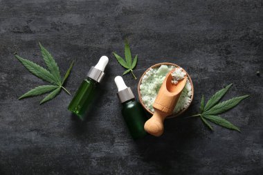 Deniz tuzu ve siyah arka planda yapraklarla kenevir kozmetik yağı şişeleri.