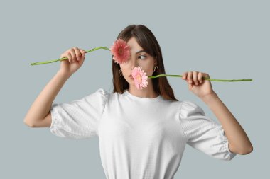 Gri arka planda pembe Gerbera çiçekleri olan güzel genç bir kadın.