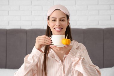 Yatak odasında kahve içen, uyku maskeli güzel genç bir kadın.