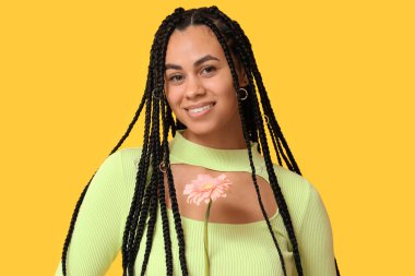 Sarı arka planda gerbera çiçeği olan güzel bir Afro-Amerikalı kadın.