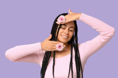 Mor arka planda kasımpatı çiçekleri olan güzel bir Afro-Amerikalı kadın.