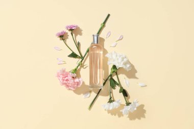 Bej arka planda bir şişe parfüm, çiçekler ve taç yaprakları.