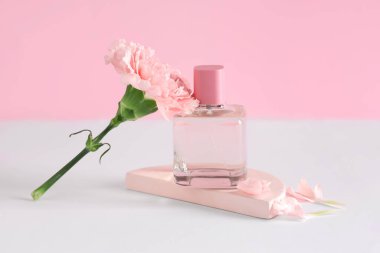 Bir şişe parfüm, alçı standı ve pembe arka planda karanfil çiçeği.