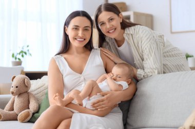 Evdeki küçük bebekleri kanepede oturan genç lezbiyen çift.