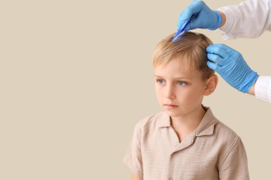 Bej arka planda pedikülozu olan küçük çocuğun saçını tarayan bir kadın doktor.