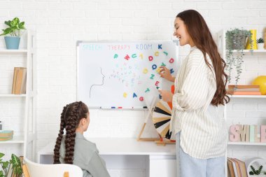 Ofiste beyaz tahtanın yanında küçük bir kızla çalışan kadın konuşma terapisti.