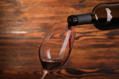 Ahşap zemin üzerinde kırmızı şarap şişesinden cama dökülüyor.