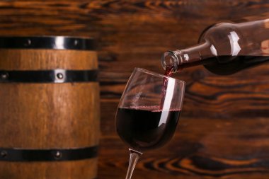 Ahşap zemin üzerinde kırmızı şarap şişesinden cama dökülüyor.