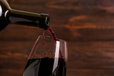 Ahşap zemin üzerinde kırmızı şarap şişesinden cama dökülüyor.