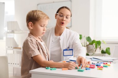 Female speech therapist working with little boy in office clipart