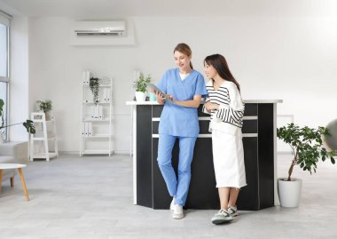 Kliniğin resepsiyonunda panosu ve hastası olan bir kadın stajyer.