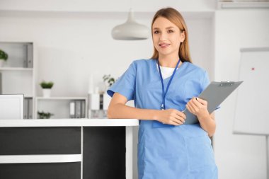 Klinikte resepsiyonun yanında panosu olan bir kadın stajyer.