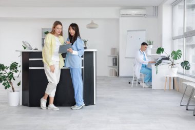 Kliniğin resepsiyonunda Asyalı bir kadın stajyer hasta ile çalışıyor.