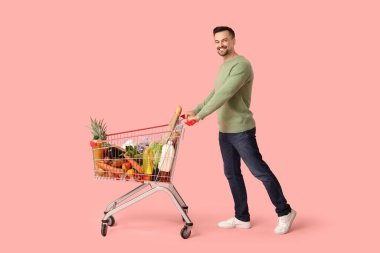 Pembe arka planda alışveriş arabası olan mutlu genç bir adam.