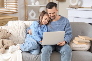 Mutlu baba ve kızı dizüstü bilgisayarlı evde kanepede oturuyor.