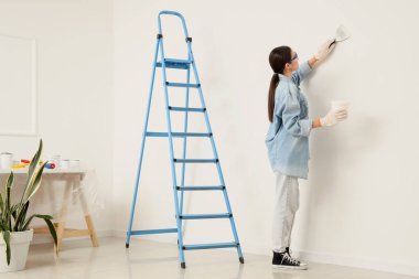 Oyun bıçağı ve kovası olan genç bir kadın beyaz duvarın yanında çalışıyor.