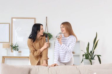 Evde mikrofonlu güzel genç kadınlar karaoke yapıyor.