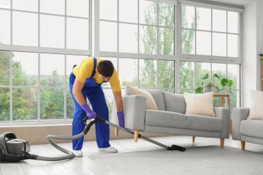 Odadaki kanepenin altındaki halıyı süpüren hademe.