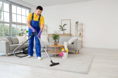 Kapıcı odada halı süpürüyor.