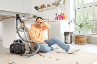 Genç adam mutfakta halı süpürdükten sonra dinleniyor.