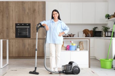 Mutfakta elektrikli süpürgesi olan genç bir kadın.