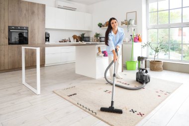 Mutfakta halı süpüren genç bir kadın.