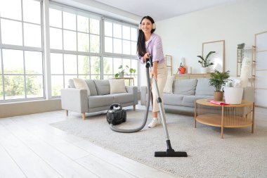 Odada müzik dinlerken halıyı süpüren genç bir kadın.