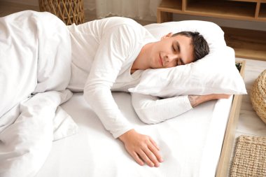 Genç adam evdeki rahat yatakta uyuyor.