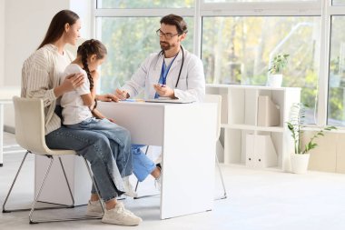 Termometre tutan erkek çocuk doktoru ve annesi klinikte hasta bir kız.