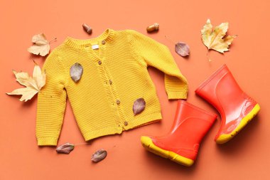 Şık bebek kıyafetleri, lastik çizmeler ve arka planda düşmüş yapraklarla kompozisyon