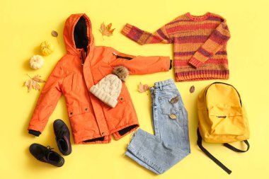 Şık çocuk kıyafetleri, ayakkabıları, aksesuarları ve sarı arka planda düşmüş yaprakları olan kompozisyon