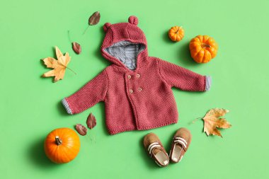 Şık bebek kıyafetleri, paçaları, balkabakları ve yeşil arka planda düşmüş yaprakları olan kompozisyon