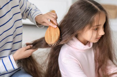 Genç anne banyoda küçük kızının saçını tarıyor, yakın plan.