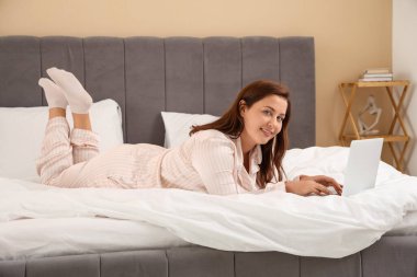 Sabahları dizüstü bilgisayarı olan güzel genç bir kadın yatakta yatıyor.