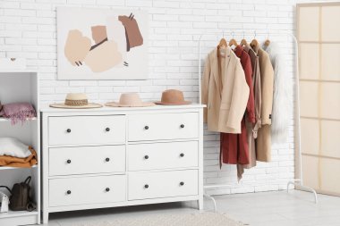 Hafif tuğla duvarın yanındaki çekmecelerde kadın kıyafetleri ve şapkalarla dizilin.