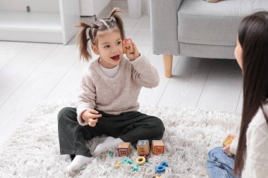 Küp ve öğretmeniyle evde halıda alfabe öğrenen sevimli küçük kız.