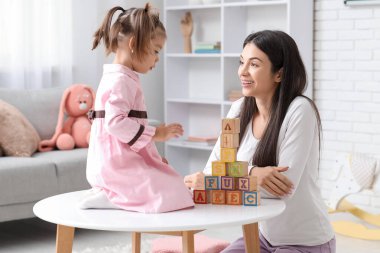 Küplü kadın öğretmen ve evde alfabe öğrenen küçük kız.