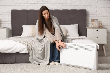Yatak odasındaki elektrikli konteyner ısıtıcısının yanında ekoseli elleri olan genç bir kadın.