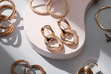 Gri arka planda farklı altın küpeleri olan dekoratif podyum