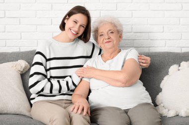 Genç hemşire ve yaşlı kadın evde kanepede kucaklaşıyorlar.