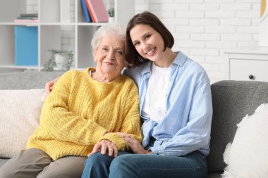 Genç hemşire ve yaşlı kadın evde kanepede kucaklaşıyorlar.