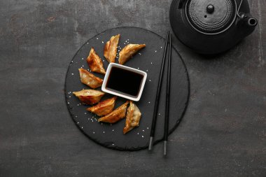 Bir kase soya soslu kızarmış Japon gyozası ve siyah arka planda çaydanlık.