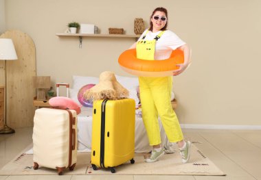 Yatak odasında yüzme yüzüğü ve bavulu olan genç bir kadın. Seyahat kavramı