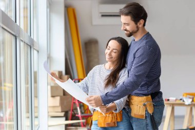 Yeni evlerinin tamiri sırasında pencere kenarında planları olan genç bir çift.