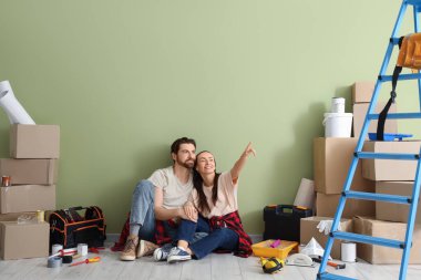 Odadaki yeşil duvarın yakınındaki bir şeyi gösteren tamir aletleri olan genç çift.